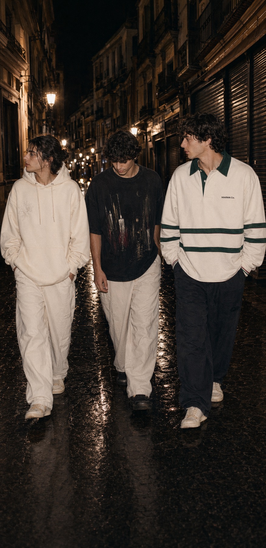 Three friends walking through a wet Sevilla street at night wearing the Azahar hoodie, Madruga tee, and Caseta rugby shirt.