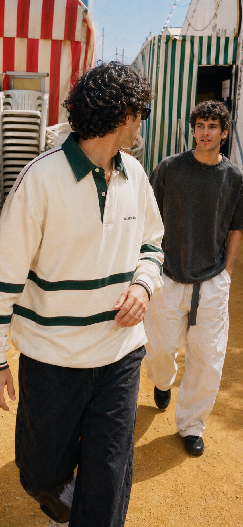 Man wearing the Caseta rugby shirt walking through a Feria backstreet with stacked chairs and albero dust.